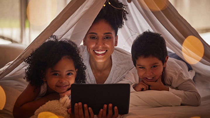 A mother watches PBS KIDS Read-Alongs on a tablet with her young daughter and son.