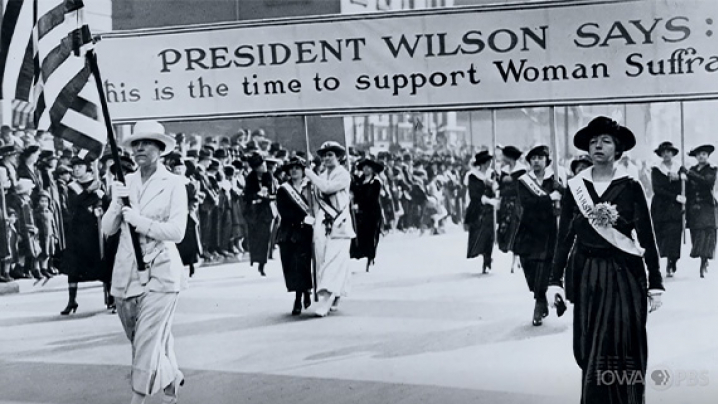 Women marching for suffrage holding a banner that says President Wilson says this is the time to support Woman Suffrage.