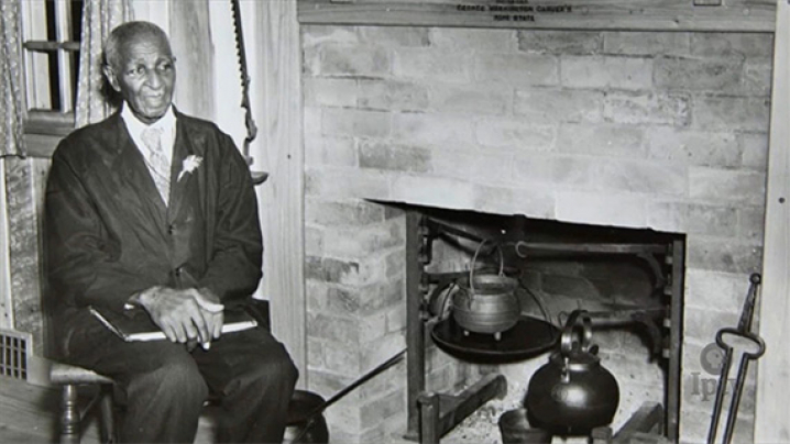 George Washington Carver is sitting in front of a fireplace.