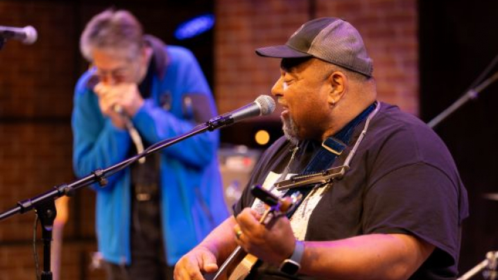 Blues artist Kevin Burt singing into a microphone with blues artist Bob Dorr on the harmonica.