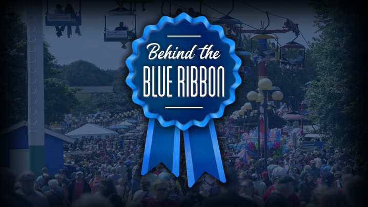 Crowded fairground with a large blue ribbon graphic displaying text.