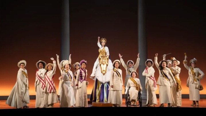 A group of women on stage with their hands raised.