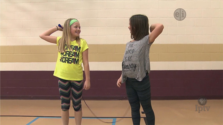Two young girls use one jump rope to jump together.