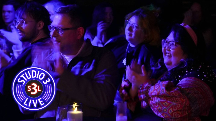 A dark event space with the audience clapping for a band.
