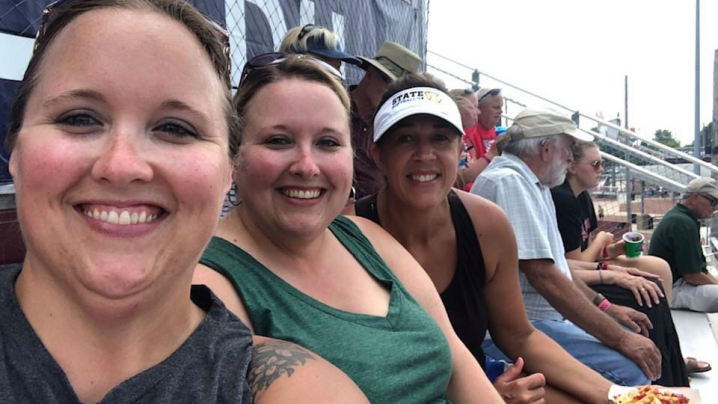 Three young women in tank tops sit in the bleachers.