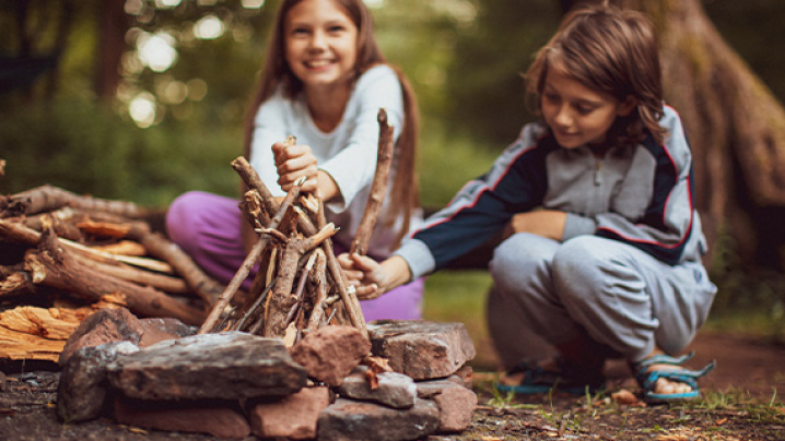 Two children building a small fire pit with sticks and rocks outdoors.