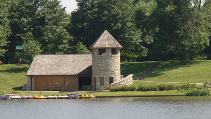 Small stone building with a turret and kayaks by a lake, surrounded by greenery.