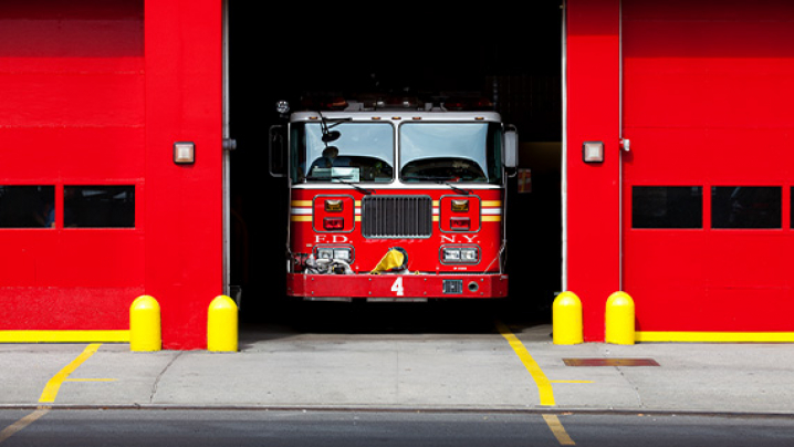 A red fire truck parked inside a fire station garage with a partially open door.