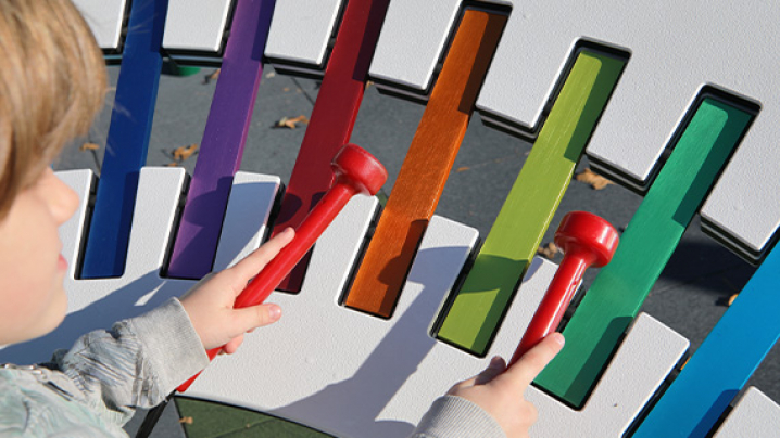 A child playing on a large rainbow colored outdoor xylophone.
