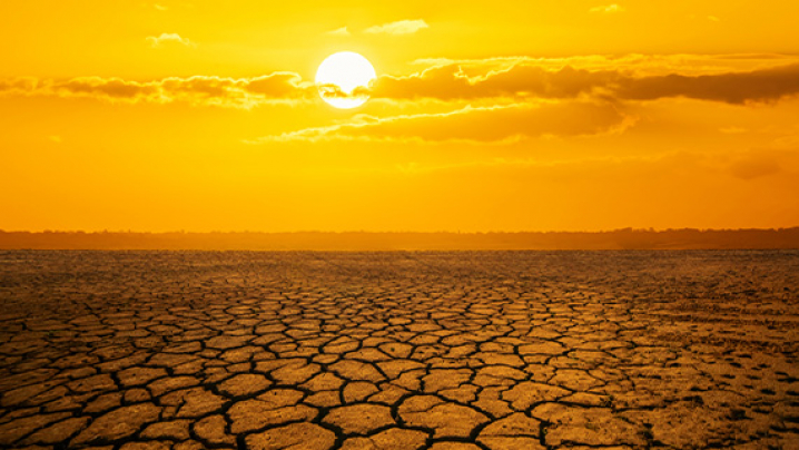 The sun shinning in a bright orange sky over land that is dry, weathered and cracked.