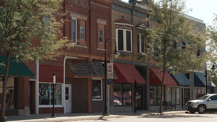 A row of historic storefronts with colorful awnings and brick facades on a tree-lined street.