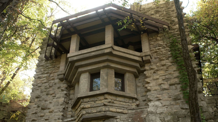A stone house with a bay window with a bay patio above.