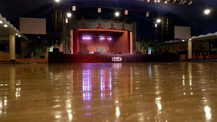 A large wood dance floor leads to a warmly lit stage.