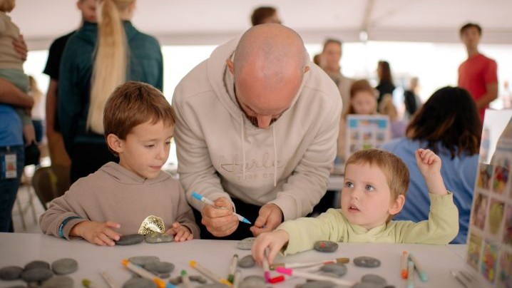 A man and two children painting kindness rocks at a table.