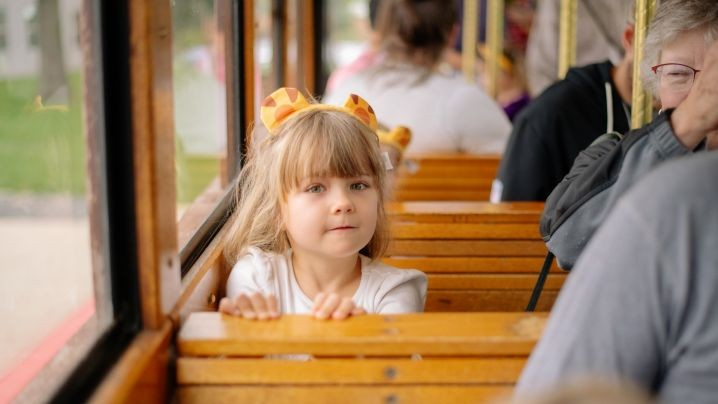 A girl with a Daniel Tiger headband on her head sitting in a trolley seat.