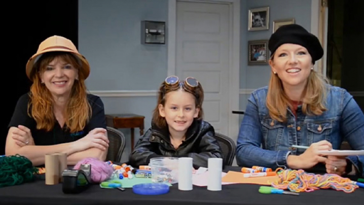 Three people sit at a table with colorful craft supplies, smiling toward the camera.
