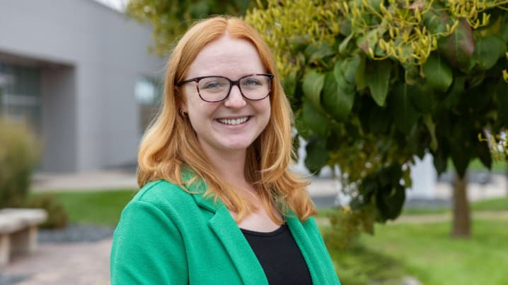 Portrait of Emily Kestel, a smiling woman wearing glasses and a bright green blazer outdoors.