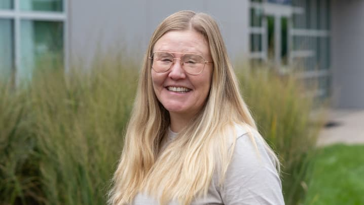 A woman with long blond hair standing outside in front of a plant. 