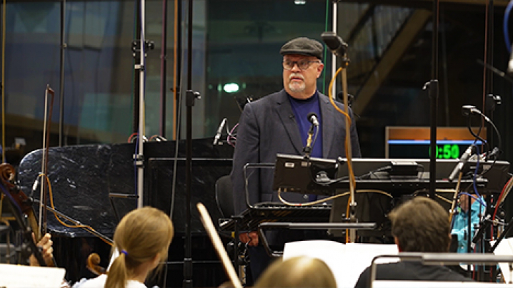 Jamie Poulsen stands on the podium before an orchestra at Abbey Road Studios.