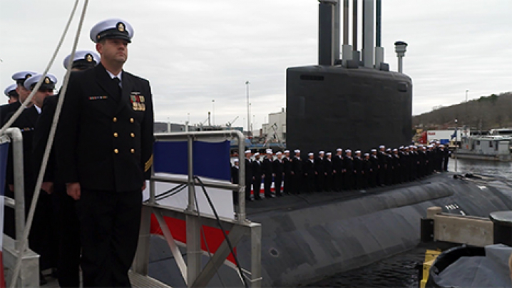 Uniformed members of the U.S. Navy stand at attention on and near the docked U.S.S. Iowa submarine.