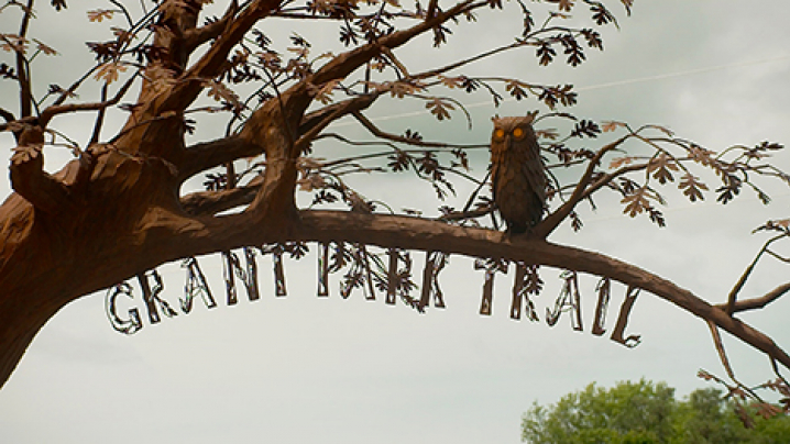 A metal sculpture of an owl on a tree with the words, "GRANT PARK TRAIL" underneath a tree branch.