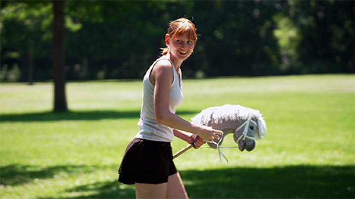 Gwen Maiers smiles and looks over her right shoulder while holding her hobby horse in a big open grassy park.