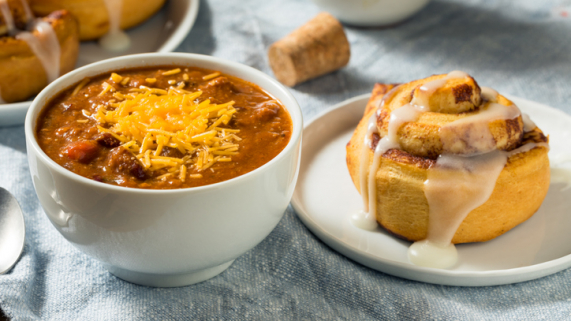 bowl of chili with cinnamon roll beside it on table
