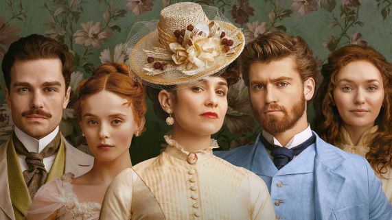 Five people in vintage clothing stand in front of floral wallpaper.