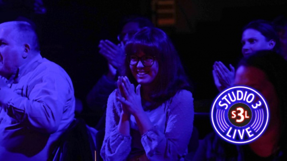 A dark event space with a woman clapping for a band.