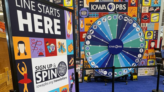 A giant prize wheel sits in front of a Fair icons backdrop.