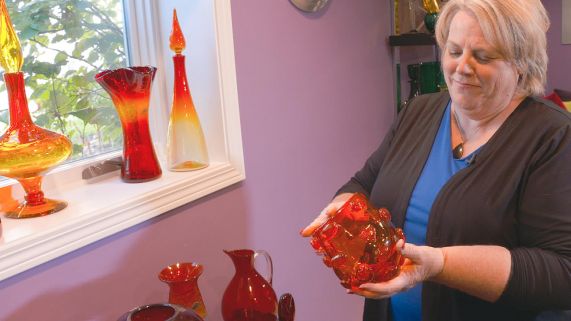 Woman holds a red glass vase from her display.