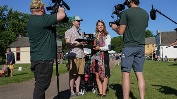 A behind-the-scenes look at the production of Antiques Roadshow - Two cameramen document a man and woman holding an old sewing machine.