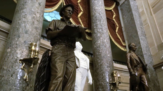 A hall with statues and marble columns, featuring draped red curtains with gold fringes.