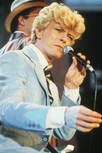 Singer, David Bowie performs onstage holding a microphone in his left hand with an outstretched right hand.