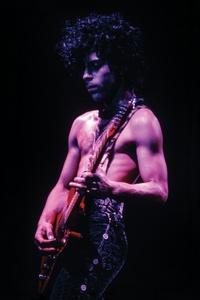 Prince Rogers Nelson, more commonly known mononymously as Prince (an American singer-songwriter, musician, and record producer) performs shirtless onstage while playing his guitar.
