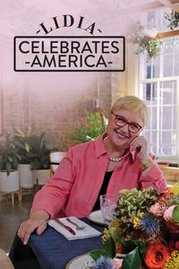 Beloved chef and Italian immigrant, Lidia Bastianich sits at a table smiling at the camera with her head resting on her left hand.