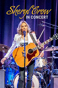 Sheryl Crow plays her guitar onstage in front of her drummer.