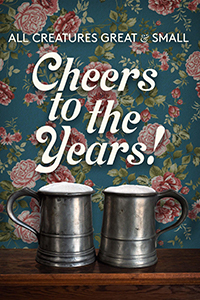 All Creatures Great and Small: Cheers to the Years! - two pints of beer on a wooden surface with a pink rose wallpaper pattern behind everything.
