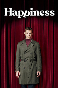 Happiness logo at the top. A red stage curtain at the back. A man (Charlie Summers) in an army green trench coat and maroon turtleneck stands still with arms at his side while he looks off to his left.