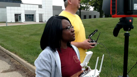 A high school student standing with an Iowa PBS staffer and learning to use a drone