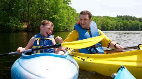 A boy and a man smiling while sitting in kayaks on a lake.