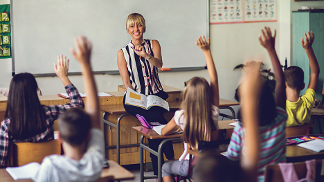 A smiling teacher calling on her students who have their hands raised.