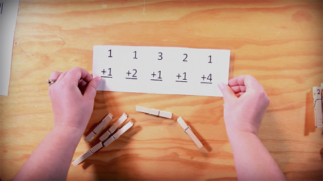 A set of hands holding a math sheet to be used with clothespins.