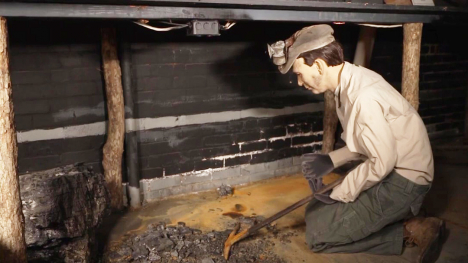 A manikin of a coal miner crouched over a pile of coal. 