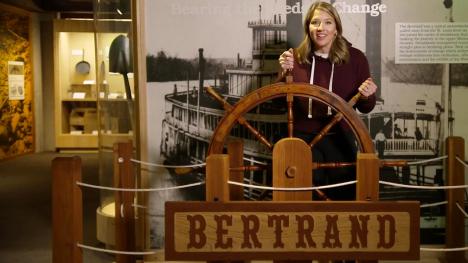 Abby Brown behind a replica wooden steering wheel to a steamboat.