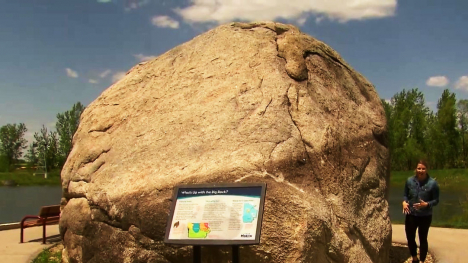 Abby Brown standing beside a massive boulder which is more than twice as tall as she is.