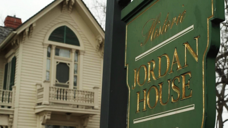 A view of the Jordan House in the background with the identification sign for the Jordan House in the foreground.