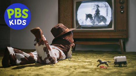 A nostalgic photo of a boy in a cowboy costume laying on the floor watching his favorite cowboy TV program.