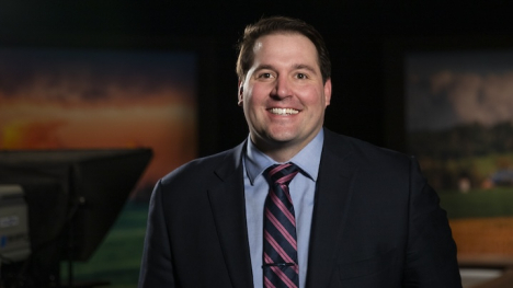 An image of Andrew Batt, a white man with short brown hair. Batt is wearing a black suit jacket with a light blue shirt and a red and navy striped tie. 