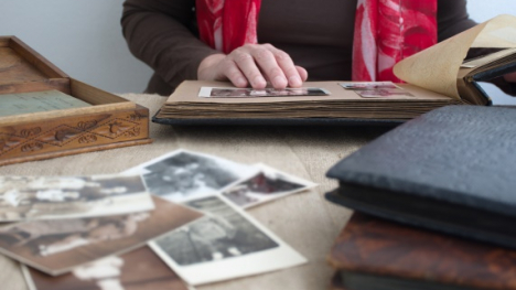 A woman looking at a family photo album with other photos on the table